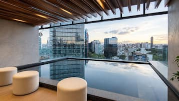 A modern rooftop terrace with a glass barrier, city skyline view, and minimalist seating.