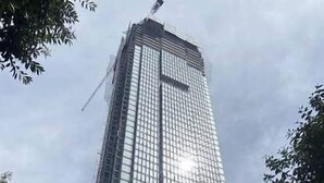 Um edifício alto e moderno com fachada de vidro, rodeado por árvores e uma estrutura azul.
