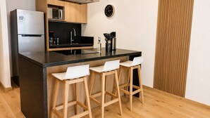 Cozinha equipada com geladeira, micro-ondas, pia e banquetas de bar.