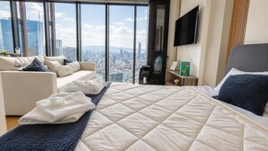 Quarto de hotel com uma cama grande, um sofá, uma TV e vista para a cidade.