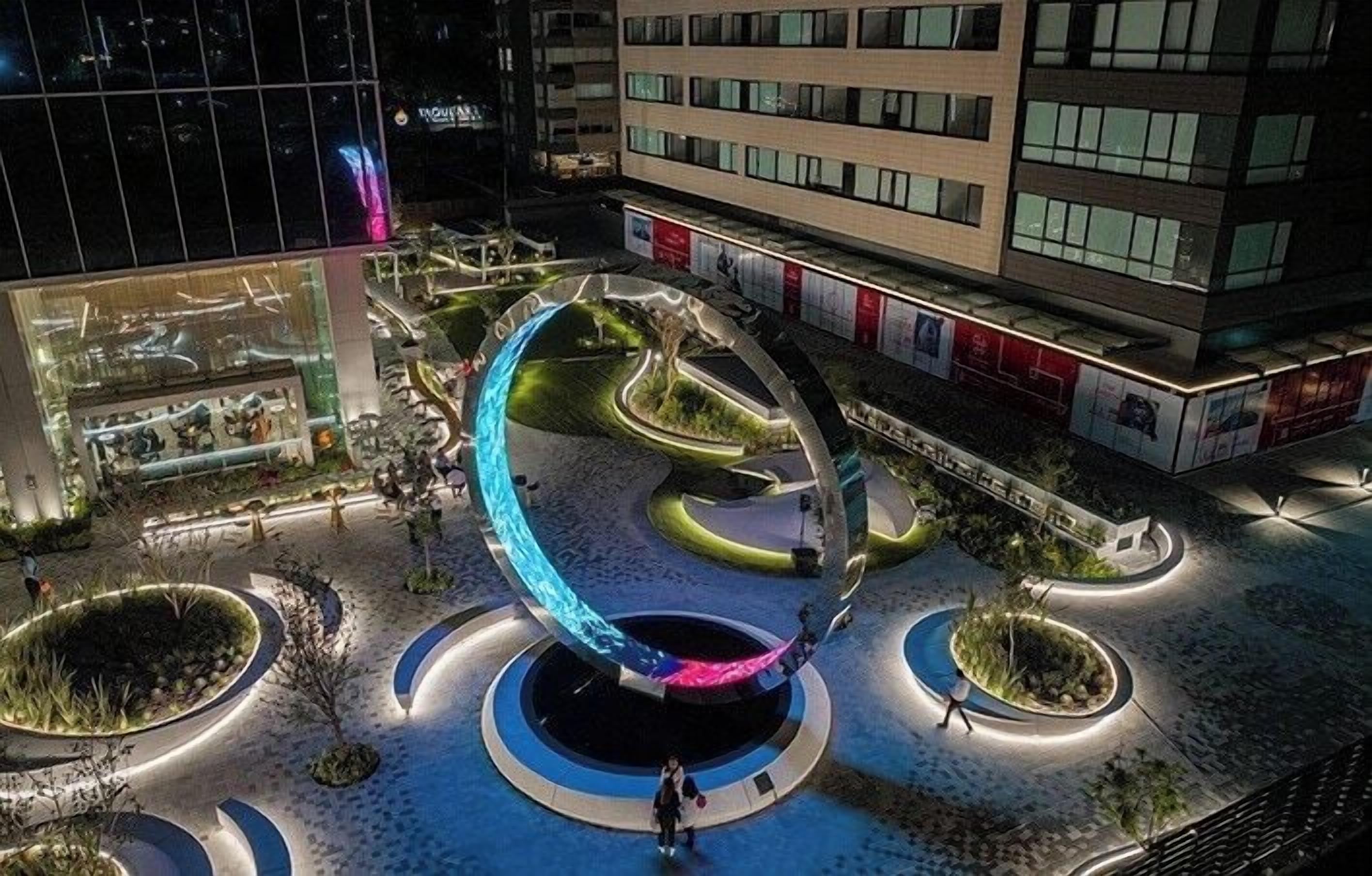 An outdoor circular structure with a central platform, surrounded by landscaped areas and pathways.