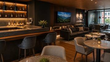 A modern bar area with a marble countertop and a selection of bottles. There is a comfortable seating area with sofas and a flat-screen TV mounted on the wall.