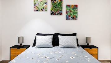 A bedroom with a bed, two nightstands, and three wall-mounted paintings.