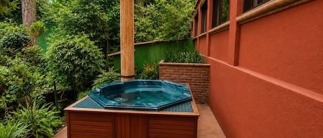 Ein Whirlpool in einem Gartenbereich mit einer Holzterrasse, umgeben von üppiger Vegetation und einer roten Mauer.