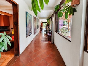 A hallway with tiled flooring, framed artwork on the walls, and a view of the outside through a window.