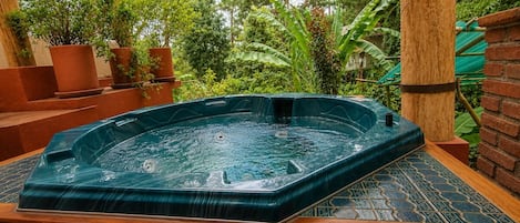 A hot tub in an outdoor setting with steps leading up to it, surrounded by greenery and a brick wall.