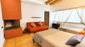 A room with a fireplace, a sofa, two beds, and a window with curtains.
