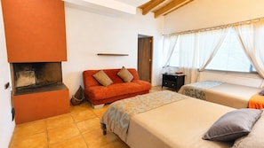 A room with a fireplace, a sofa, two beds, and a window with curtains.