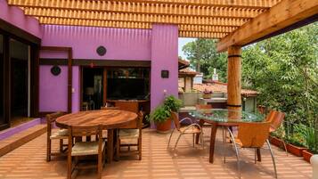 An outdoor patio with a round wooden table and chairs, surrounded by potted plants and a pergola structure.