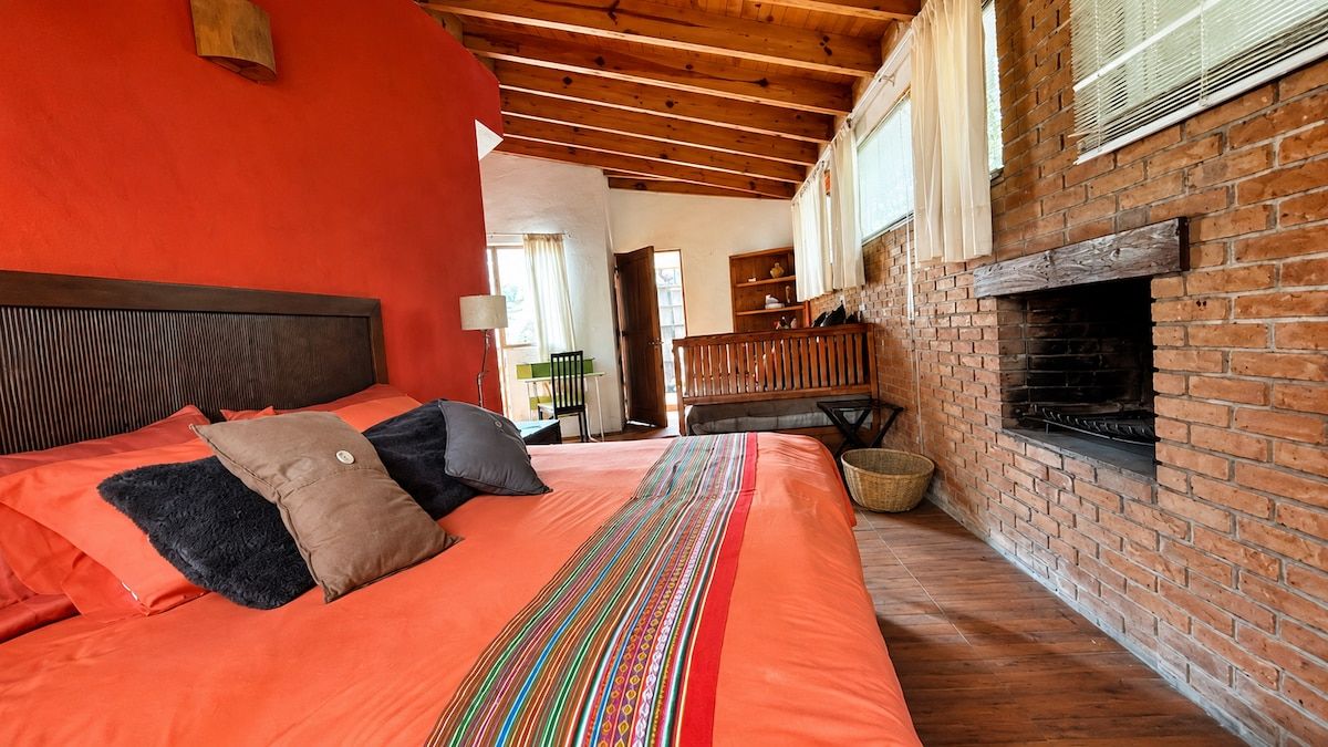 A room with a bed, a brick fireplace, and a wooden ceiling.