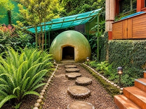 A garden pathway leading to a structure with a dome-like roof, surrounded by lush greenery and a series of wooden steps.