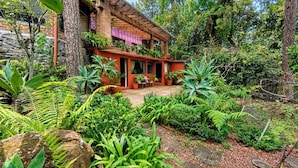 A house with a brick exterior, surrounded by lush greenery and a variety of plants. - Paloma Suite | Triple, breakfast and parking (Valle de Bravo)