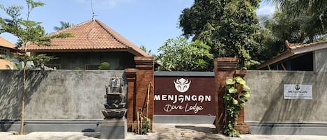 A gated entrance to Menjangan Dive Lodge with a clear sky and surrounding greenery.