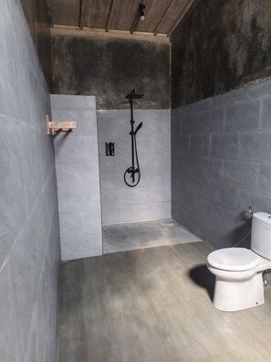 A bathroom with a shower, toilet, and a wooden shelf.
