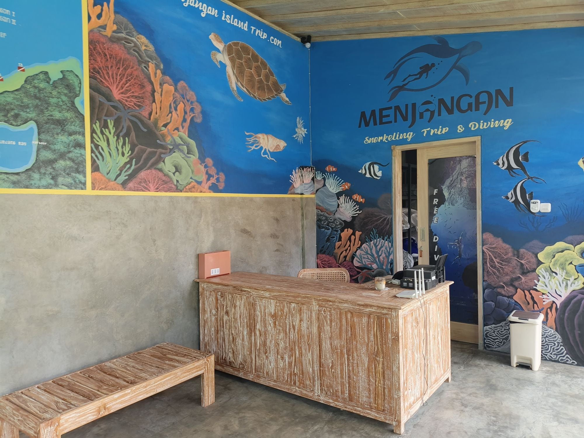 A room with a mural of marine life, a wooden desk, and a bench.
