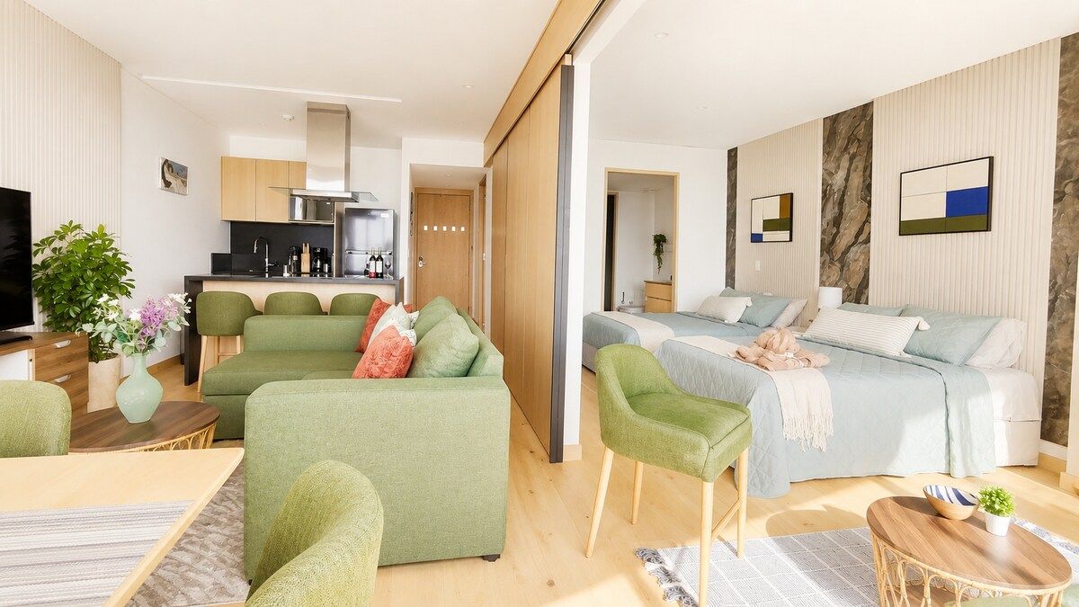 A modern living room with a sofa, a dining area, a kitchen, and a bedroom with a bed and a bedside table.