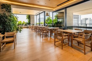 Een ruime binnenruimte met meerdere tafels en stoelen, grote ramen en kamerplanten.