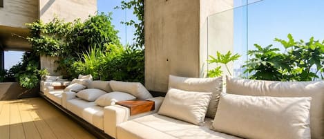 A modern outdoor seating area with a sofa and cushions, surrounded by greenery and a concrete structure.