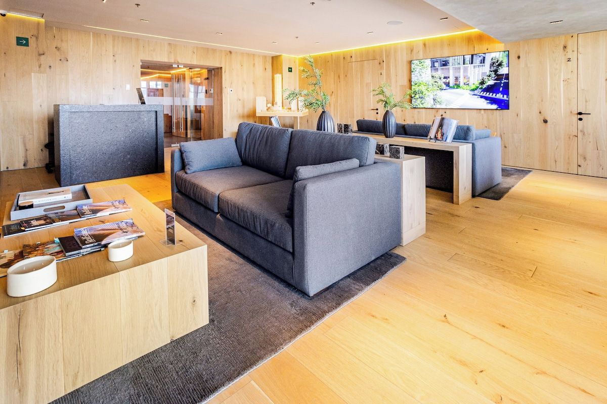 A modern lobby with a grey sofa, a wooden reception desk, and a TV screen displaying an outdoor scene.