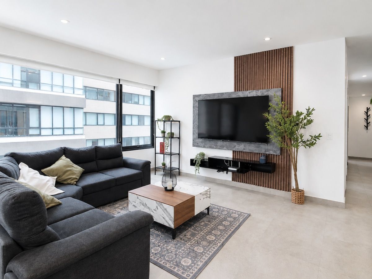 Un salon moderne avec un canapé, une table basse et un téléviseur à écran plat fixé au mur.