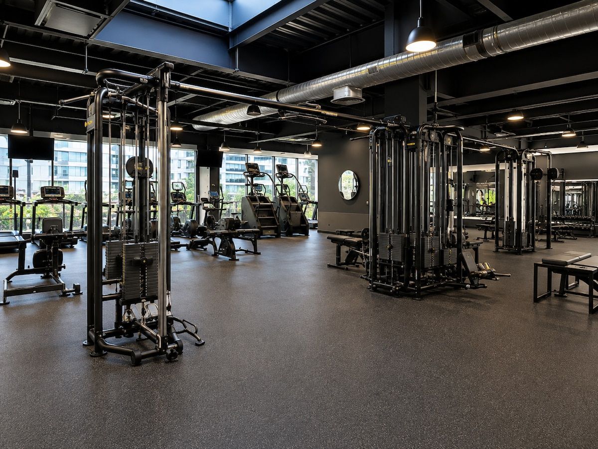 A gym with various exercise machines, large windows, and a high ceiling.