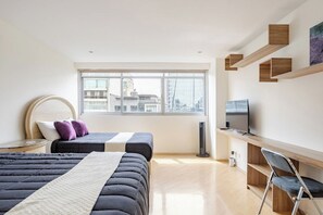 Moderni hotellihuone, jossa on kaksi sänkyä, televisio ja työpöytä tuolilla.