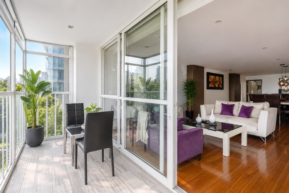 Un vaste espace de vie agrémenté d’un canapé blanc moderne, d’une table à manger et d’une grande porte-fenêtre coulissante donnant sur un balcon où sont disposées des plantes en pot.