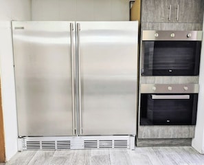 Ein Edelstahl-Kühlschrank und ein eingebauter Backofen in einer Küche mit einer Holzrückwand.