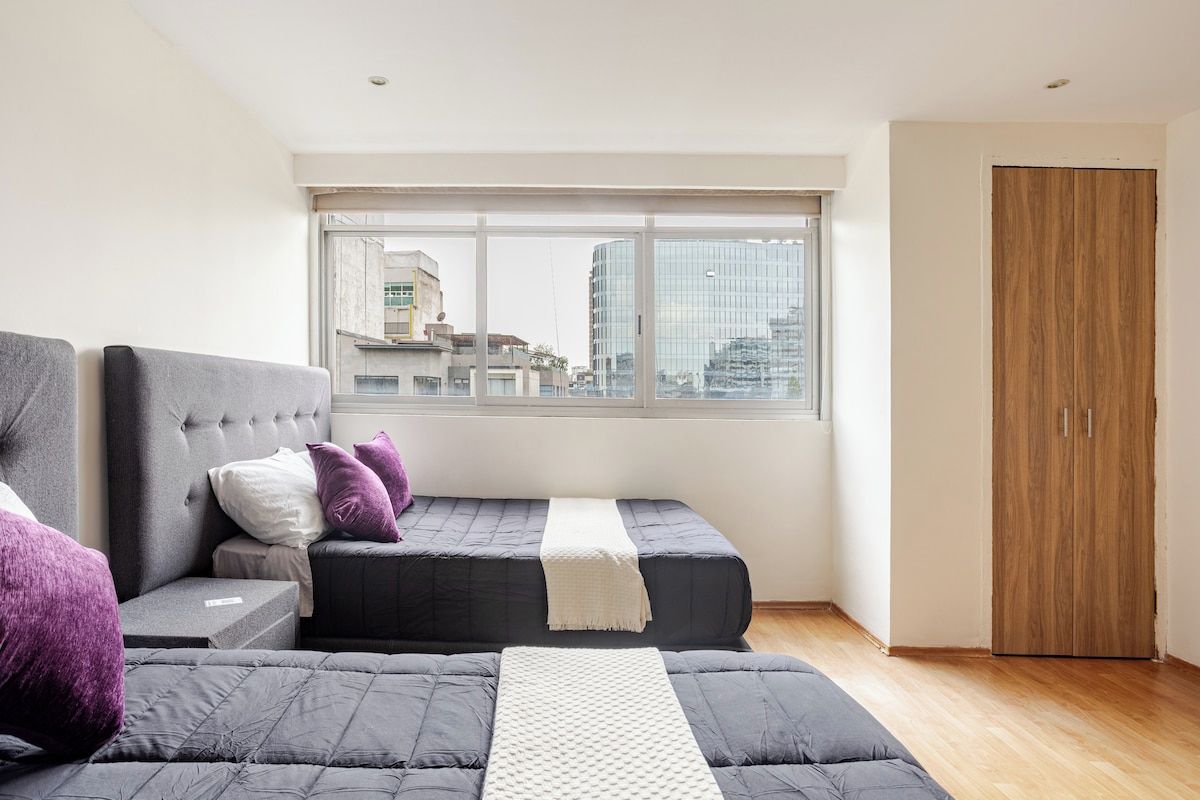 A modern bedroom with a large window, a bed with a headboard, and a wardrobe.
