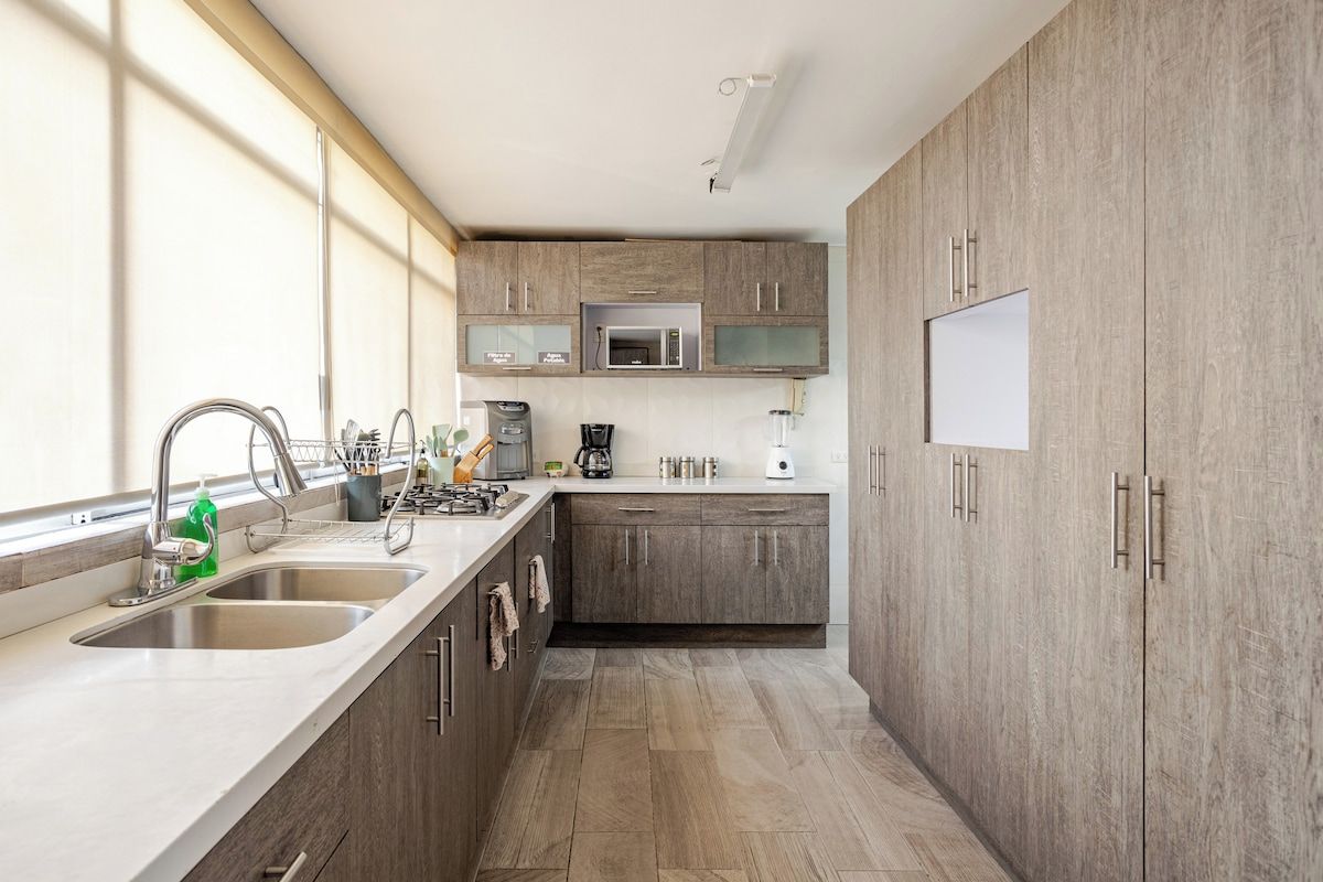 Une cuisine moderne dotée d’un îlot central, d’appareils électroménagers en acier inoxydable et de meubles de rangement en bois.