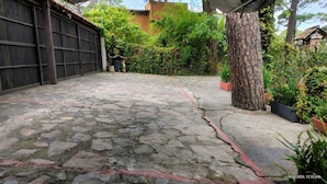 Um pátio com piso de pedra, cerca de madeira, plantas em vasos e uma árvore.