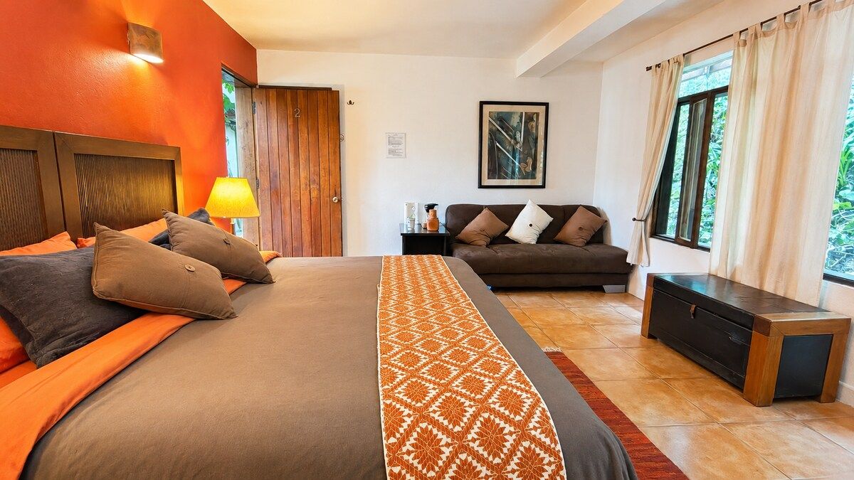A hotel room with a bed, a sofa, a nightstand, and a window with curtains.