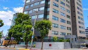 Un edificio alto y moderno con una fachada de ventanas en forma de cuadrícula, un techo plano y un cielo despejado al fondo.