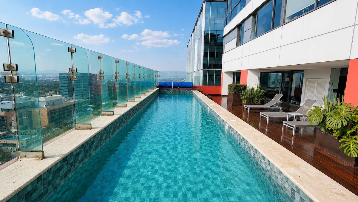 A rooftop infinity pool with glass railings, lounge chairs, and a view of the cityscape.