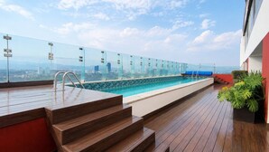 Una piscina en la azotea con barandillas de vidrio, terraza de madera y vistas a la ciudad.