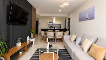 Uma sala de estar moderna com um sofá, uma mesa de centro e uma TV fixada na parede.