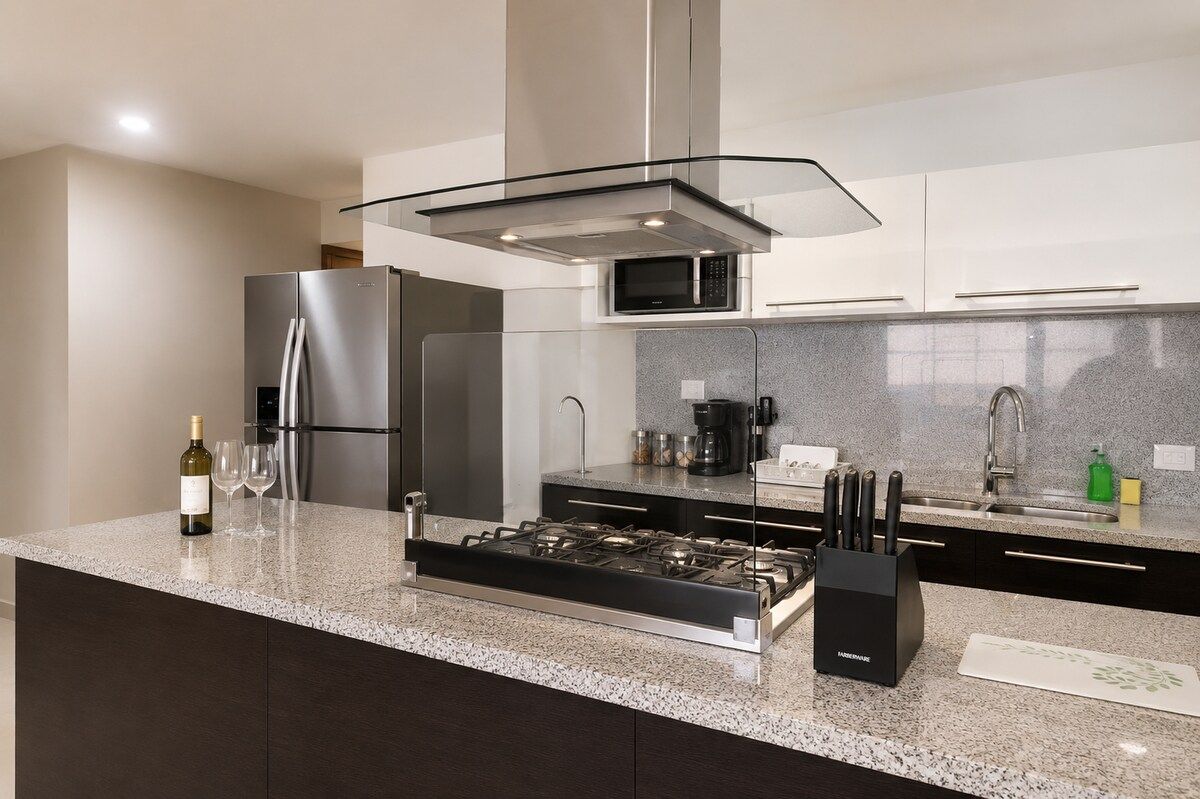 A modern kitchen with stainless steel appliances, a granite countertop, and a glass hood over the stove.