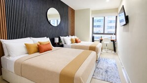 Habitación de hotel con dos camas, un escritorio, un televisor y un ventanal grande.