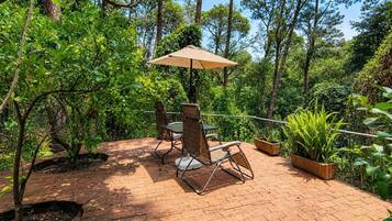 An outdoor patio with a table and chairs, surrounded by greenery and trees.