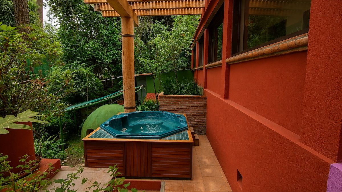 A hot tub in a garden area with a wooden deck and a bamboo pergola.