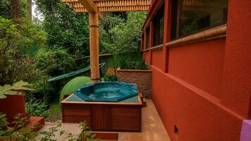 A hot tub in a garden area with a wooden deck and a bamboo pergola.