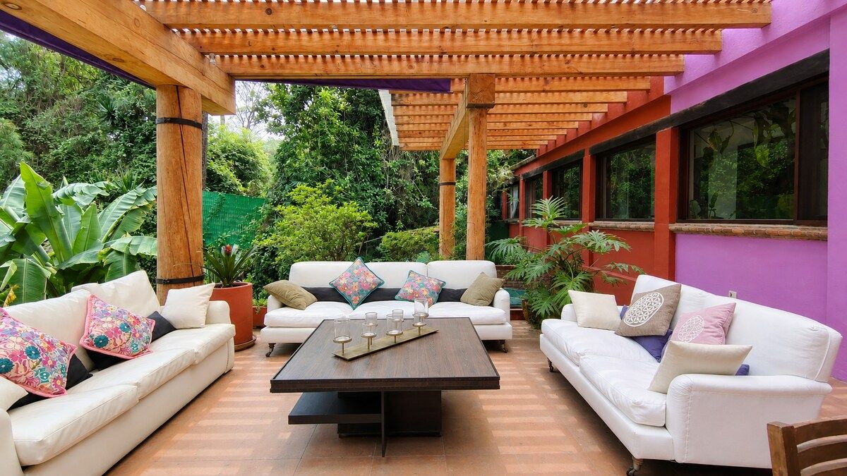 Un espace extérieur aménagé avec une zone salon couverte, comprenant deux canapés blancs, une table en bois et une structure en forme de pergola.