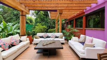 Un espace extérieur aménagé avec une zone salon couverte, comprenant deux canapés blancs, une table en bois et une structure en forme de pergola.