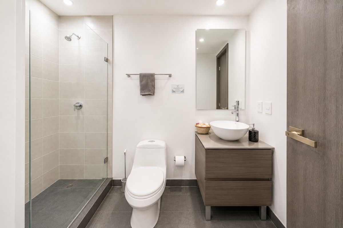 A modern bathroom with a glass shower enclosure, a toilet, a vanity with a sink, and a mirror.