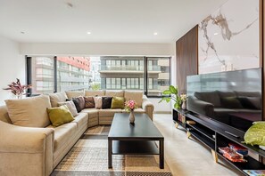 A modern living room with a sectional sofa, a coffee table, a flat-screen TV, and a large window offering a city view. - Polanco Condo: Heated Pool, Jacuzzi, Near Antara (Mexico City)
