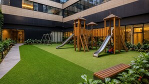 A playground with slides and climbing structures, surrounded by a well-maintained lawn and a building with large windows. - Polanco 4BR Neuchatel | Pool, Jacuzzi, Gym, Antara (Mexico City)