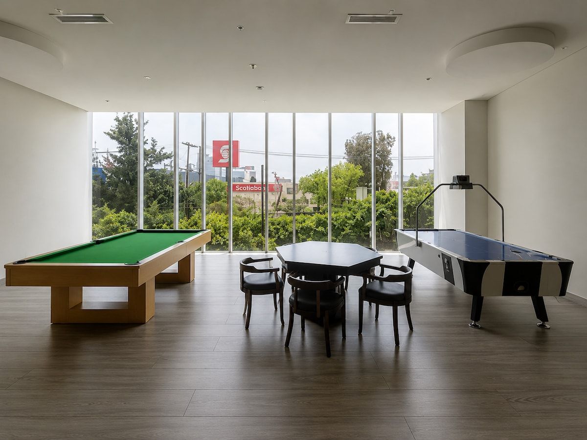 Une table de billard entourée de chaises, une autre table de billard, et une grande fenêtre donnant sur un paysage verdoyant et des bâtiments.