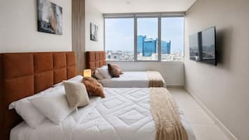 Quarto de hotel com uma janela grande, duas camas, televisão de tela plana e obras de arte nas paredes.