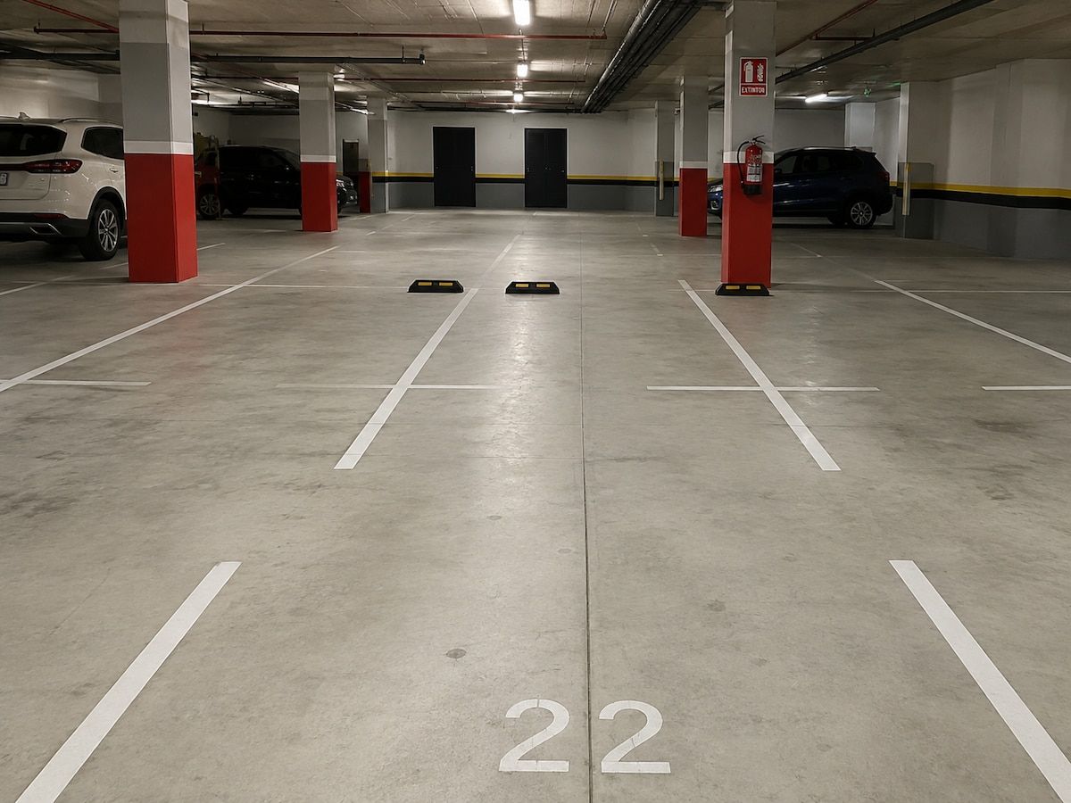 Un parking avec des piliers blancs et rouges, des places de stationnement numérotées et un extincteur sur un des piliers rouges.
