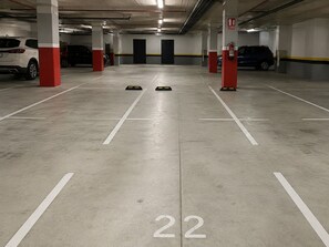 Un parcheggio sotterraneo con pilastri bianchi e rossi, posti auto numerati e un estintore su un pilastro rosso.